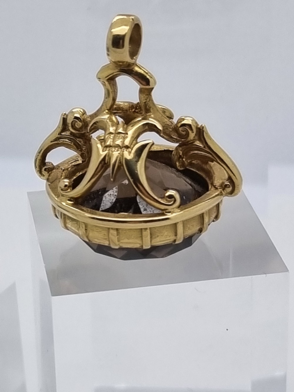 An ornate 9ct gold watch fob pendant set with a large faceted smokey quartz gemstone and detailed scrollwork frame. View II