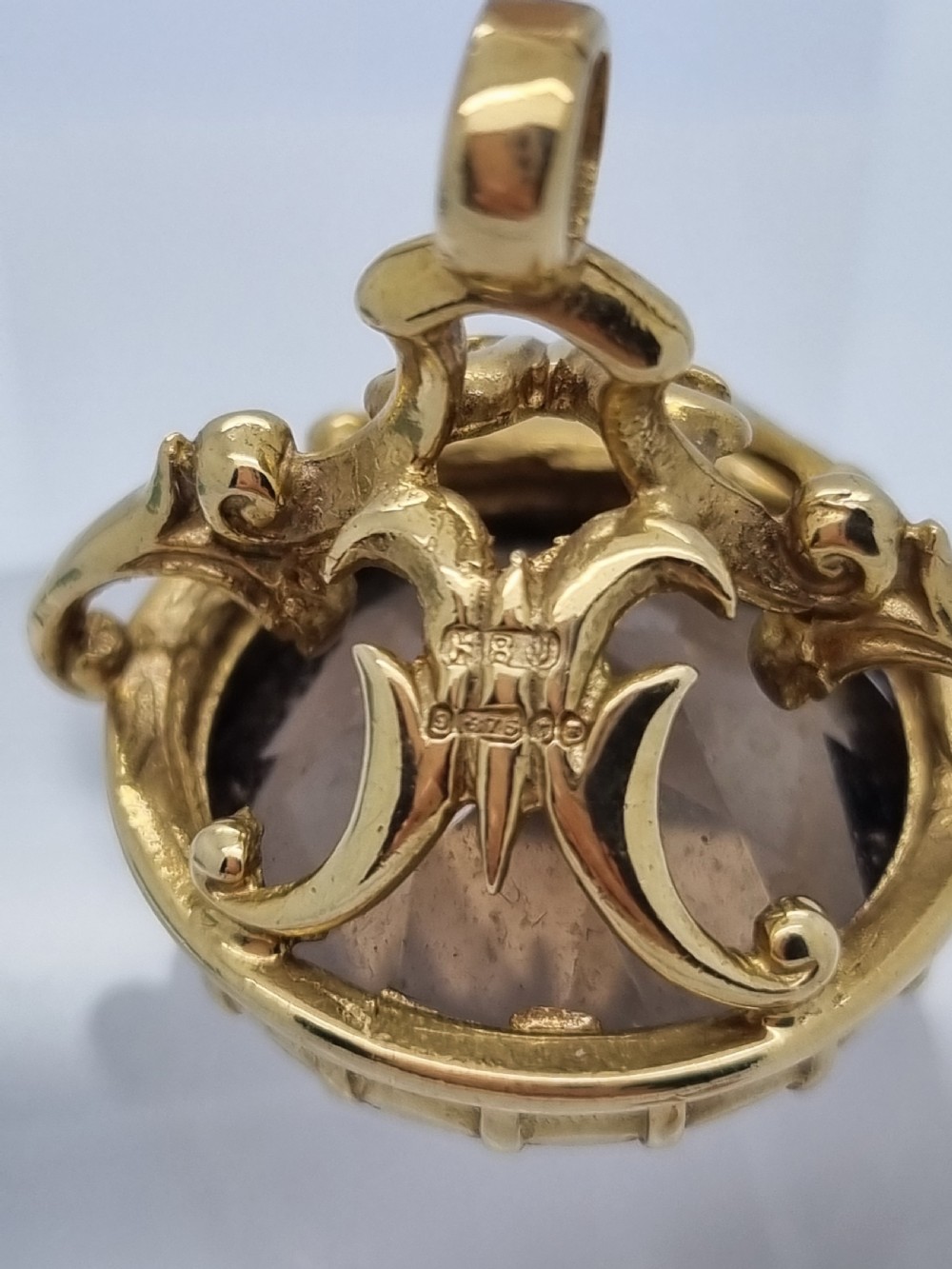 An ornate 9ct gold watch fob pendant set with a large faceted smokey quartz gemstone and detailed scrollwork frame. View IV