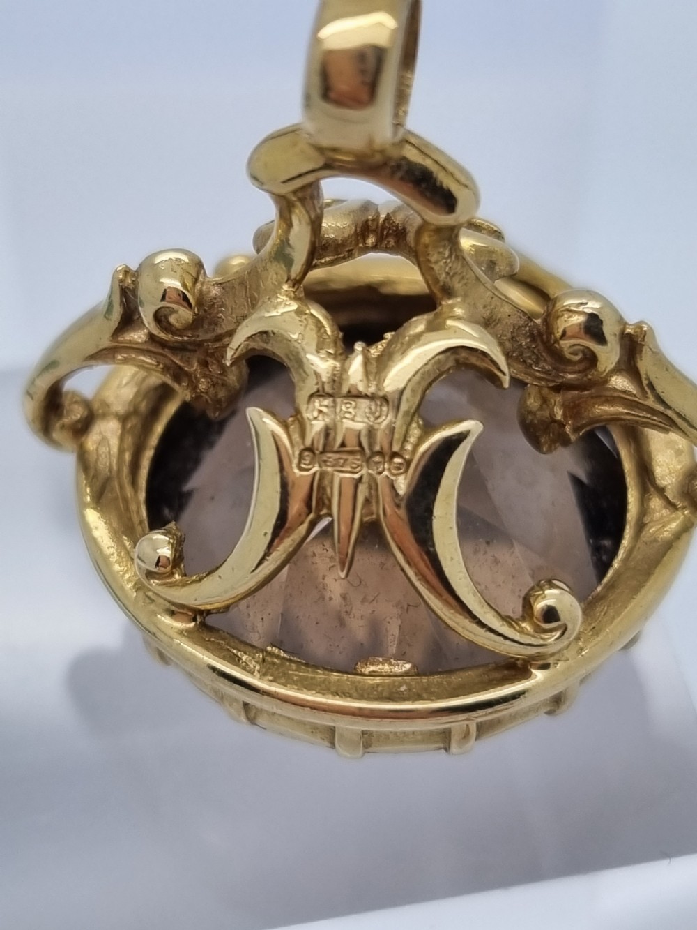 An ornate 9ct gold watch fob pendant set with a large faceted smokey quartz gemstone and detailed scrollwork frame. View V