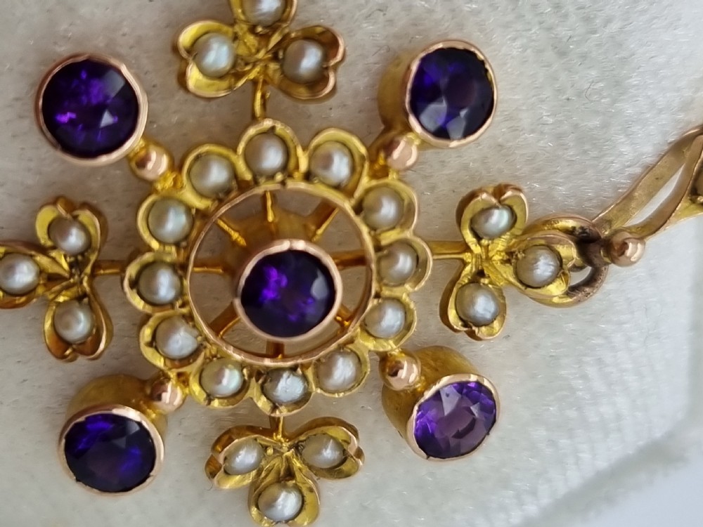 A Victorian gold starburst pendant set with round purple amethysts and delicate seed pearls hanging from a thin gold chain. View IV
