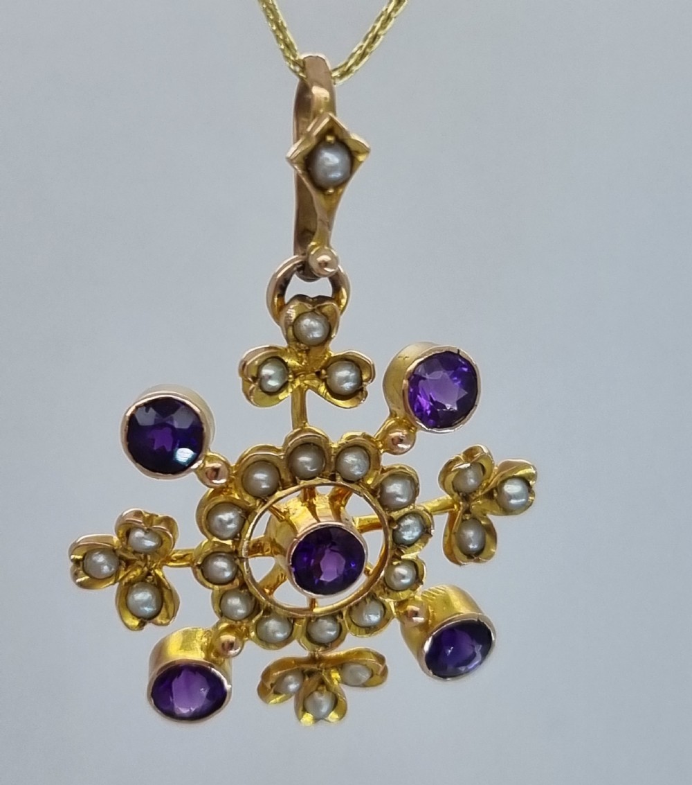 A Victorian gold starburst pendant set with round purple amethysts and delicate seed pearls hanging from a thin gold chain.
