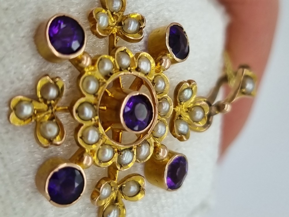 A Victorian gold starburst pendant set with round purple amethysts and delicate seed pearls hanging from a thin gold chain. View II