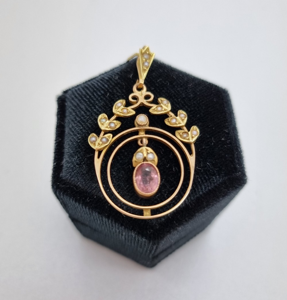 An Edwardian 15ct gold pendant featuring seed pearl leaf motifs, concentric gold rings, and a central suspended oval pink gemstone. View IV