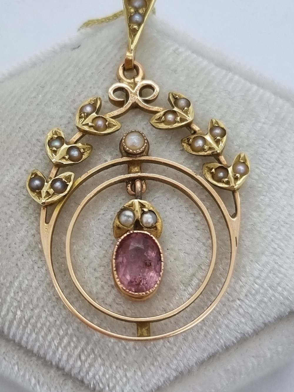 An Edwardian 15ct gold pendant featuring seed pearl leaf motifs, concentric gold rings, and a central suspended oval pink gemstone. View VII