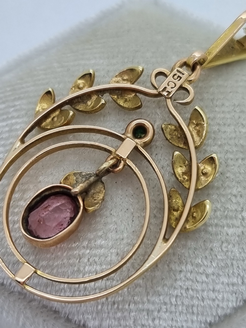 An Edwardian 15ct gold pendant featuring seed pearl leaf motifs, concentric gold rings, and a central suspended oval pink gemstone. View VIII
