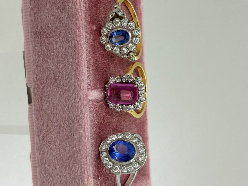 An Edwardian oval blue sapphire cluster ring surrounded by a diamond halo with foliate shoulders and a yellow gold shank. View III