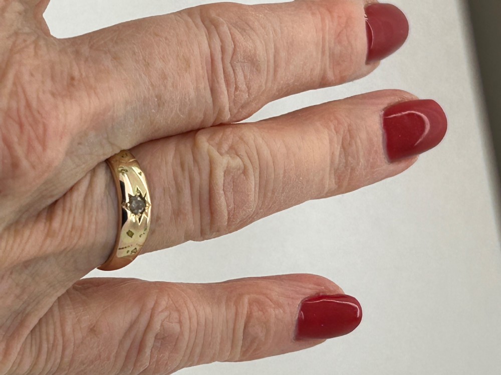 A yellow gold band ring featuring a single clear gemstone embedded within a carved starburst celestial motif. View III