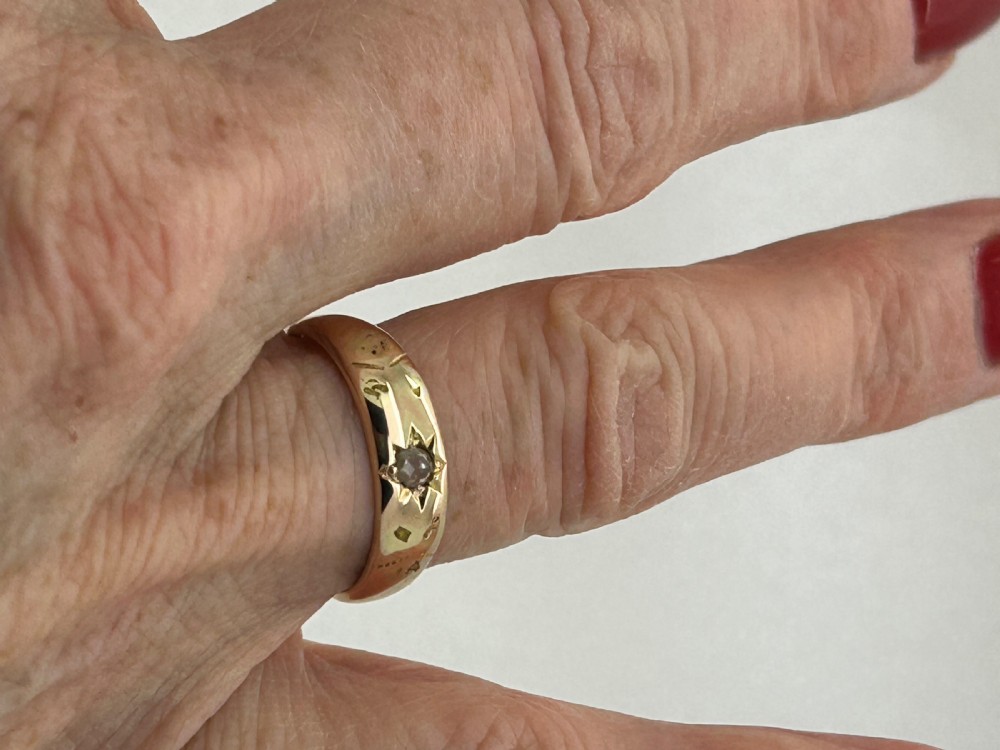 A yellow gold band ring featuring a single clear gemstone embedded within a carved starburst celestial motif. View VI