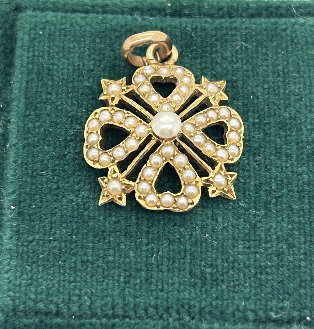 An antique Victorian openwork gold pendant set with seed pearls featuring a four-lobed heart motif with star points.