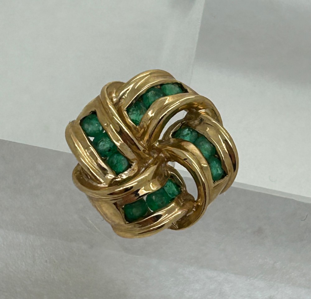 A pair of yellow gold knot earrings featuring channel-set green emerald gemstones woven into the metal bands. View III