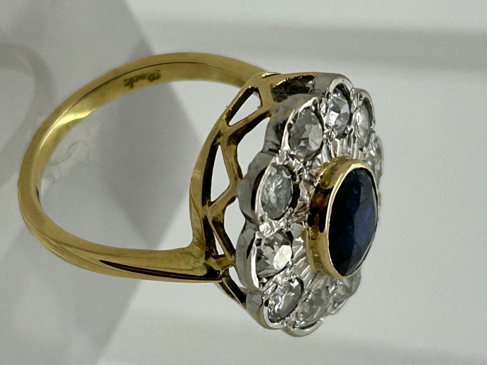 A yellow gold cluster ring featuring a central oval dark blue sapphire framed by a scalloped halo of round cut diamonds. View IV