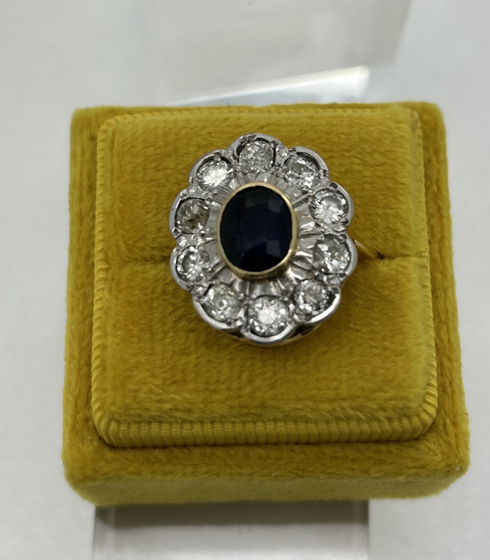 A yellow gold cluster ring featuring a central oval dark blue sapphire framed by a scalloped halo of round cut diamonds. View VIII