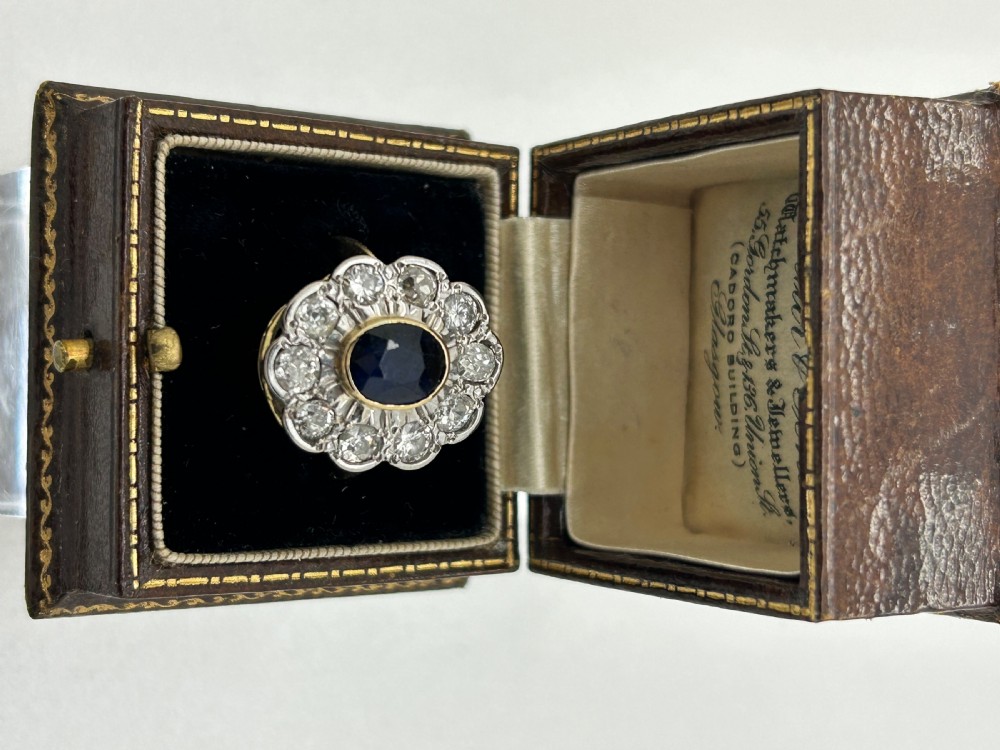 A yellow gold cluster ring featuring a central oval dark blue sapphire framed by a scalloped halo of round cut diamonds. View IX