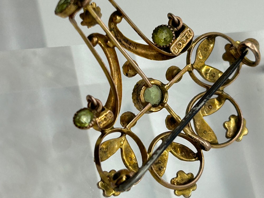 An Edwardian gold openwork pendant brooch featuring open scrolls, small seed pearls, a central faceted green peridot, and three dangling peridot droplets. View III