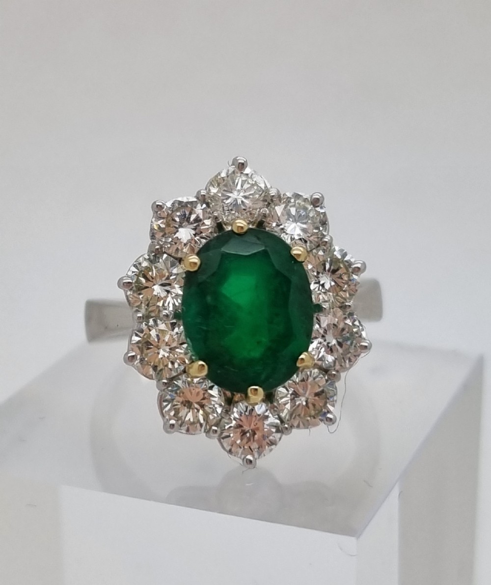 An 18ct gold ring featuring a central oval green emerald framed by a halo of round brilliant-cut diamonds.