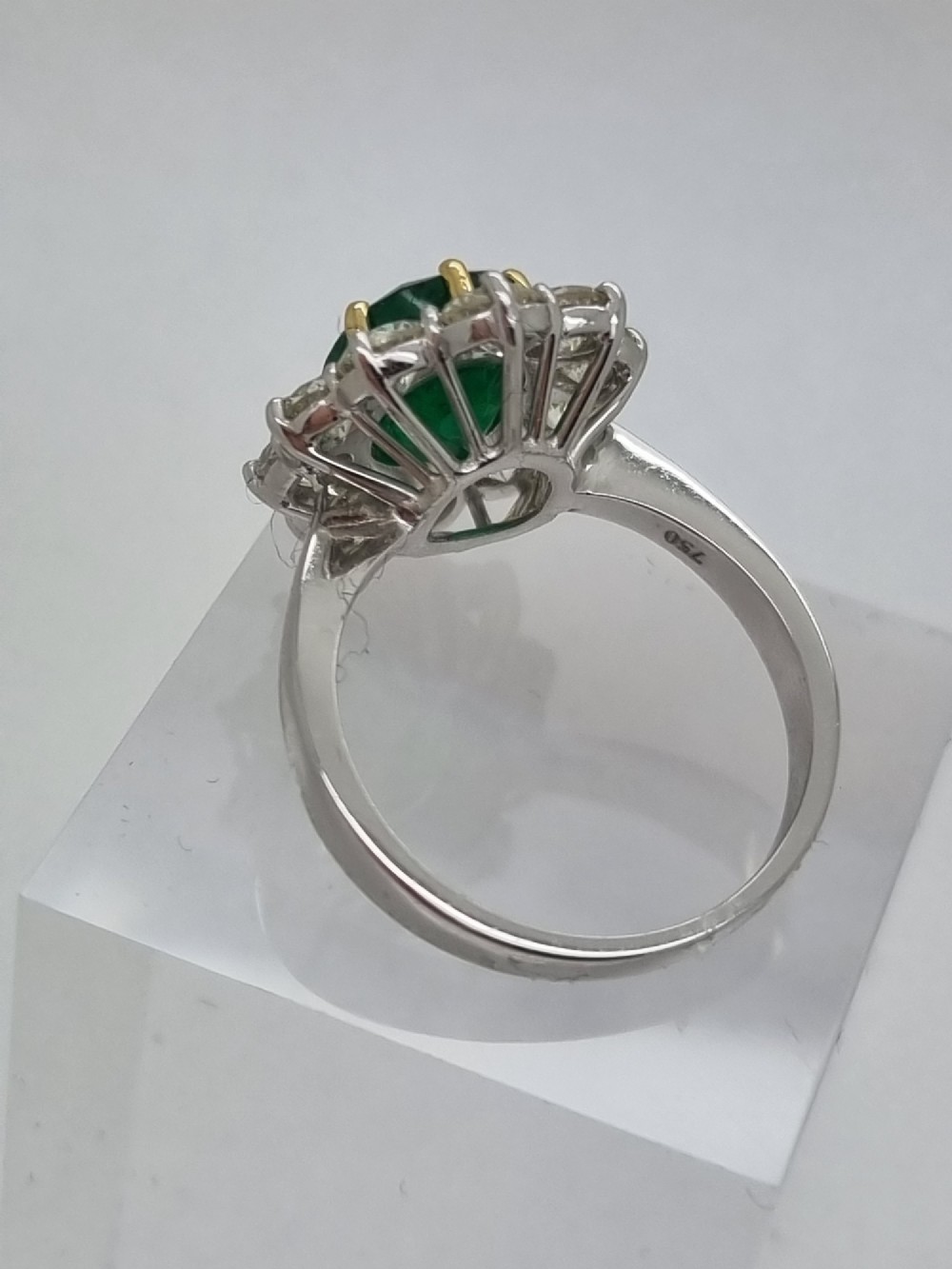 An 18ct gold ring featuring a central oval green emerald framed by a halo of round brilliant-cut diamonds. View III