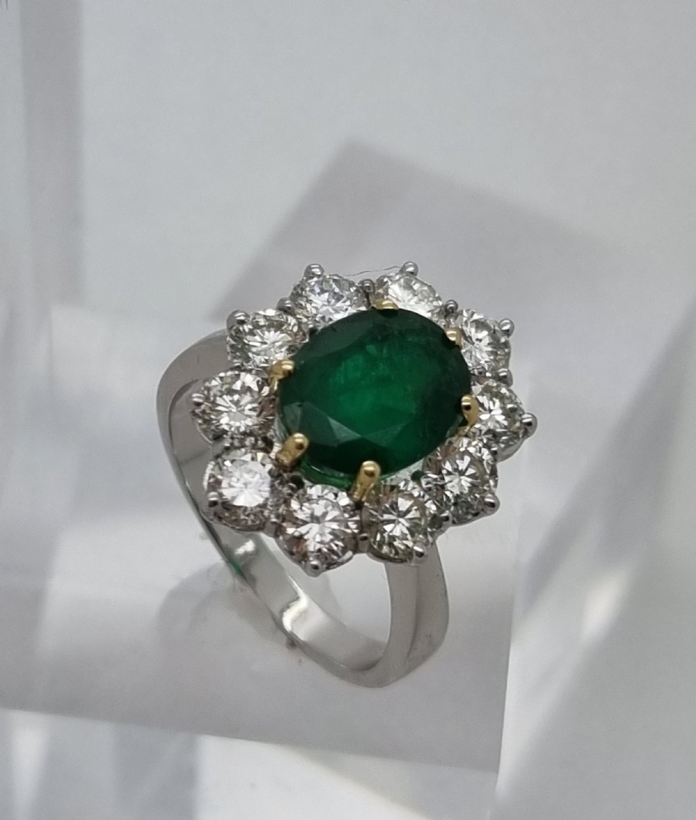 An 18ct gold ring featuring a central oval green emerald framed by a halo of round brilliant-cut diamonds. View IV