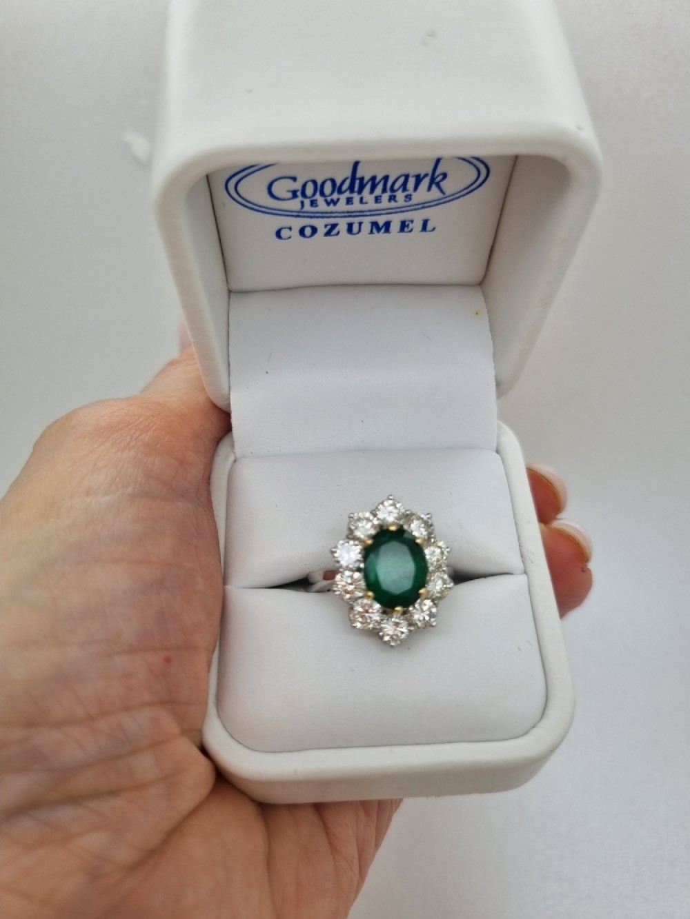 An 18ct gold ring featuring a central oval green emerald framed by a halo of round brilliant-cut diamonds. View VII