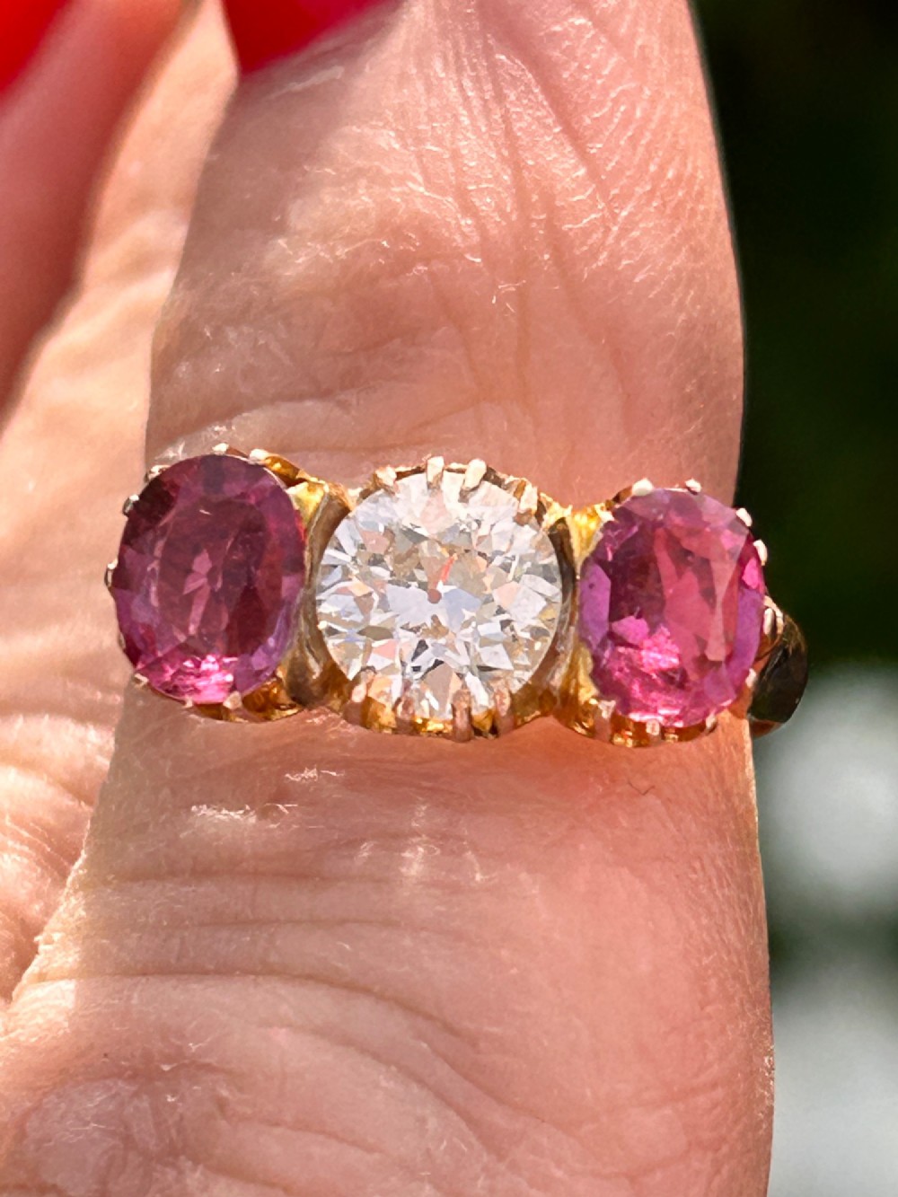 A Victorian yellow gold trilogy ring featuring a central round diamond flanked by two oval pinkish-red rubies in claw settings.