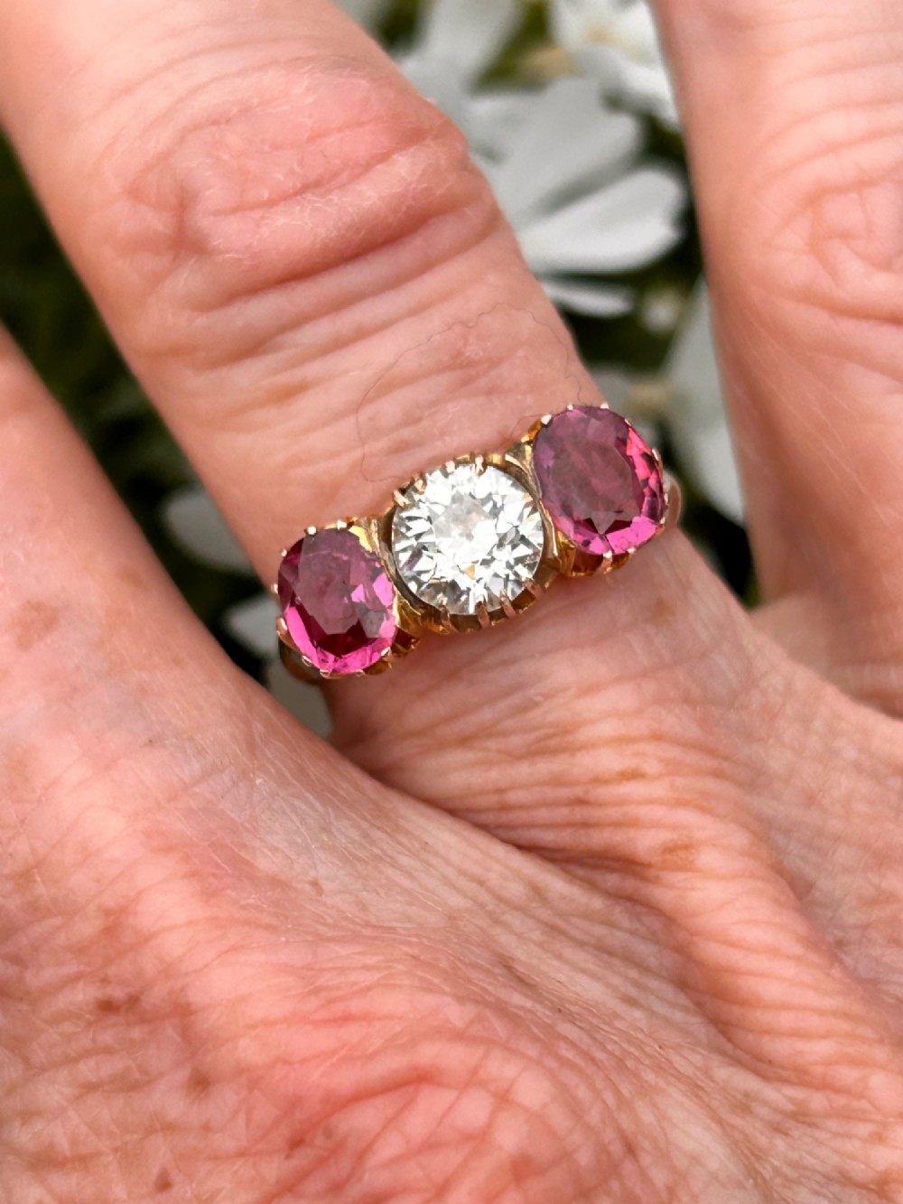 A Victorian yellow gold trilogy ring featuring a central round diamond flanked by two oval pinkish-red rubies in claw settings. View II