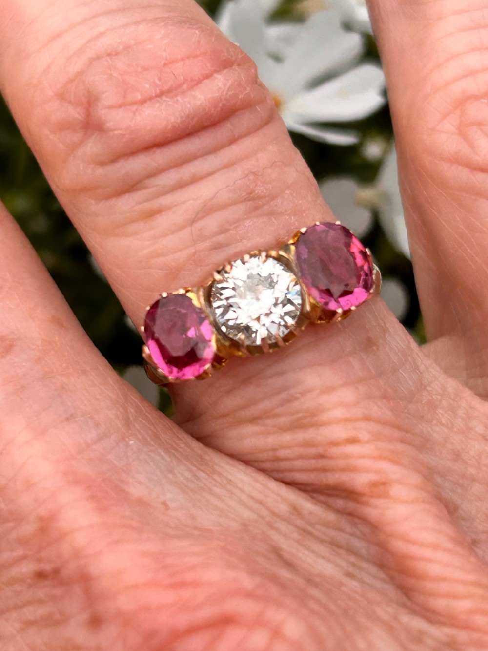 A Victorian yellow gold trilogy ring featuring a central round diamond flanked by two oval pinkish-red rubies in claw settings. View III