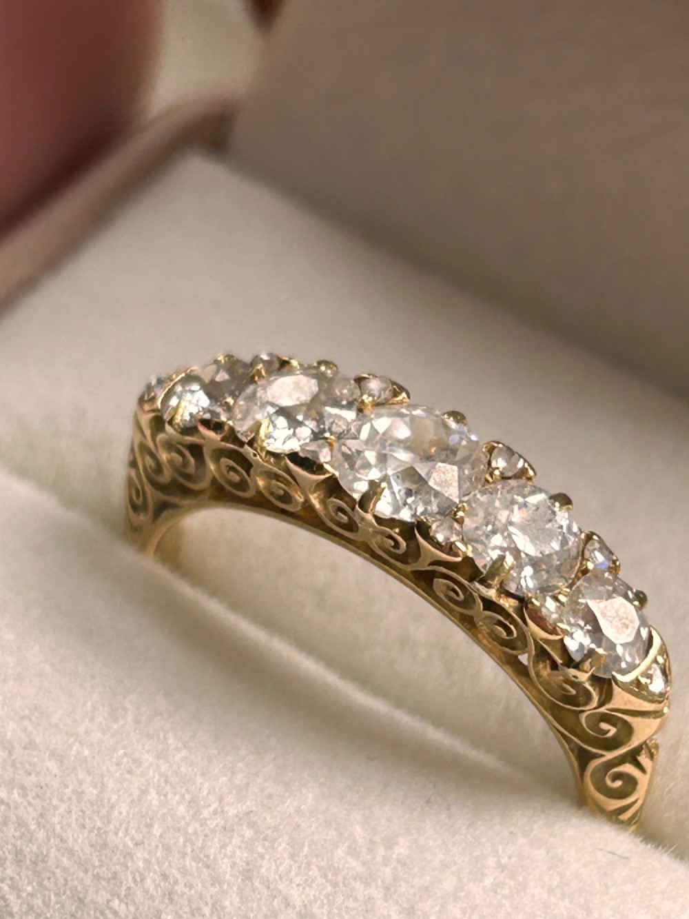 An antique Victorian gold ring featuring five graduated diamonds set into an openwork scroll gallery.
