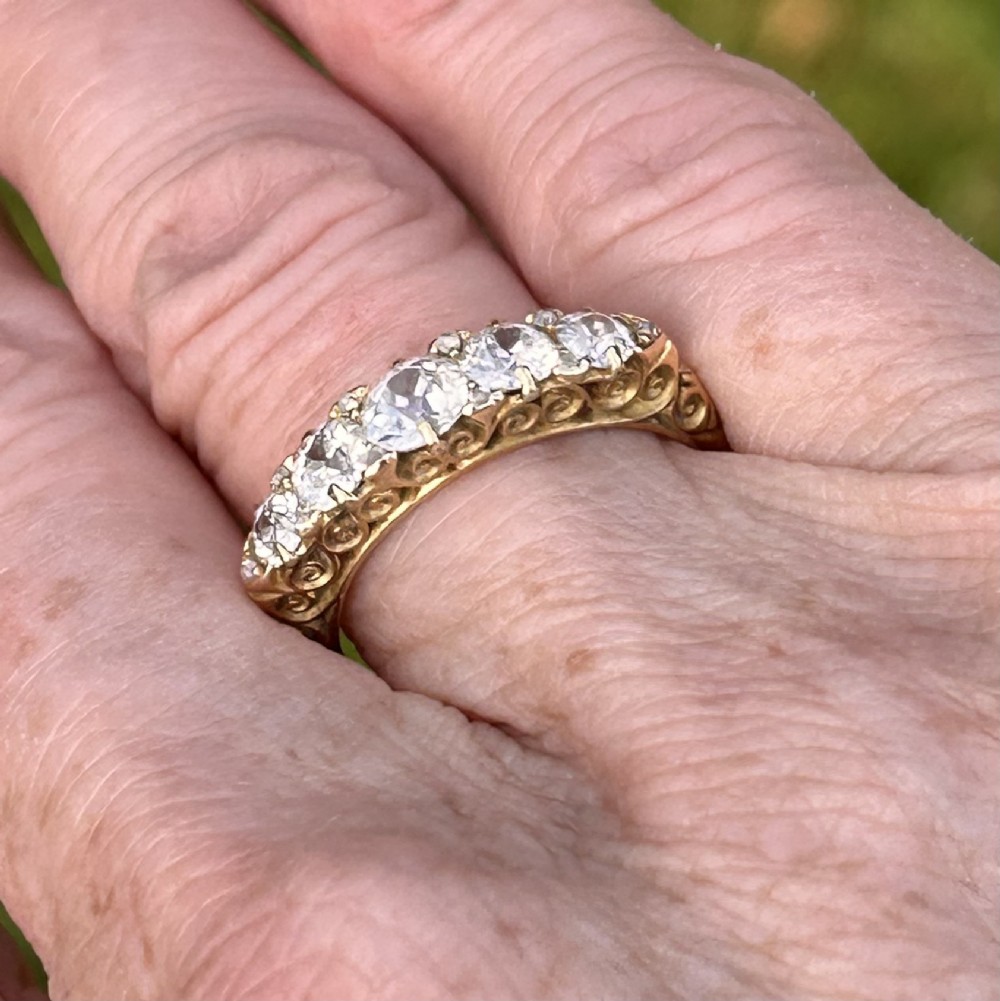 An antique Victorian gold ring featuring five graduated diamonds set into an openwork scroll gallery. View IV