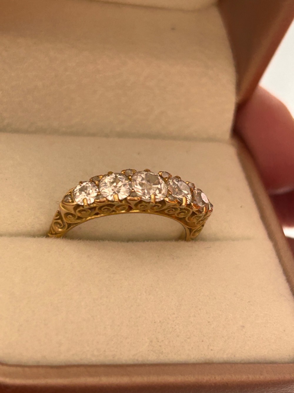 An antique Victorian gold ring featuring five graduated diamonds set into an openwork scroll gallery. View VI