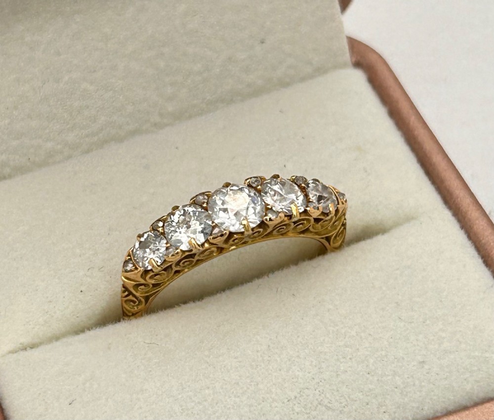 An antique Victorian gold ring featuring five graduated diamonds set into an openwork scroll gallery. View VIII