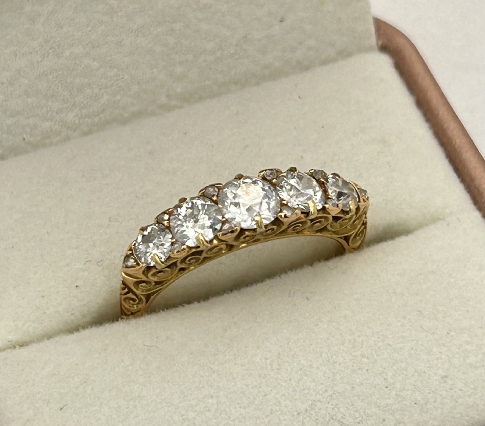 An antique Victorian gold ring featuring five graduated diamonds set into an openwork scroll gallery. View IX