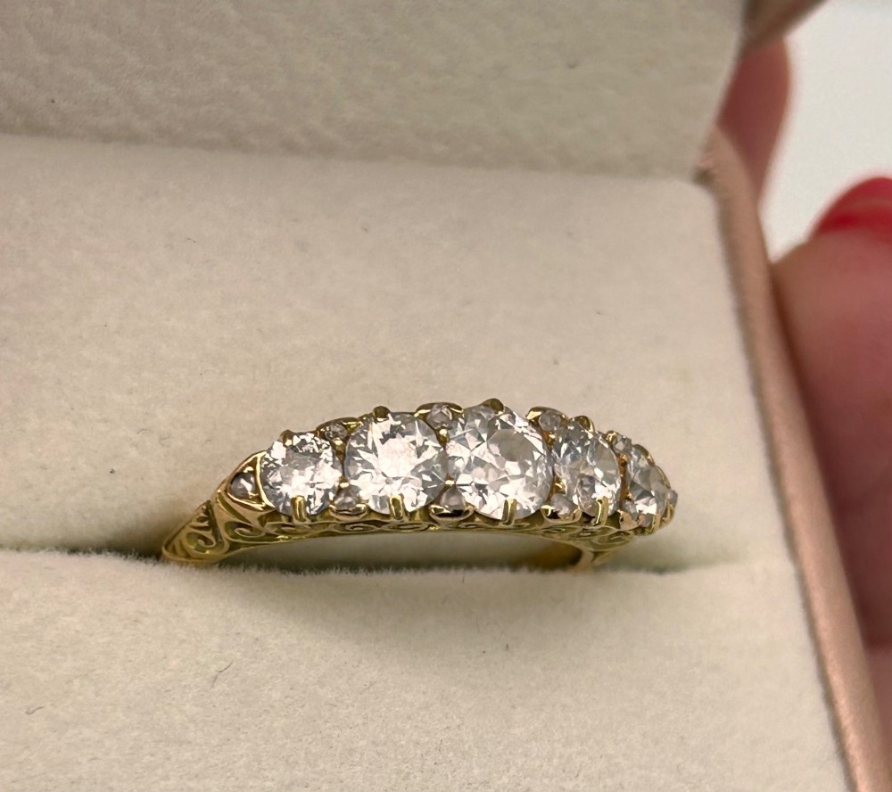 An antique Victorian gold ring featuring five graduated diamonds set into an openwork scroll gallery. View X