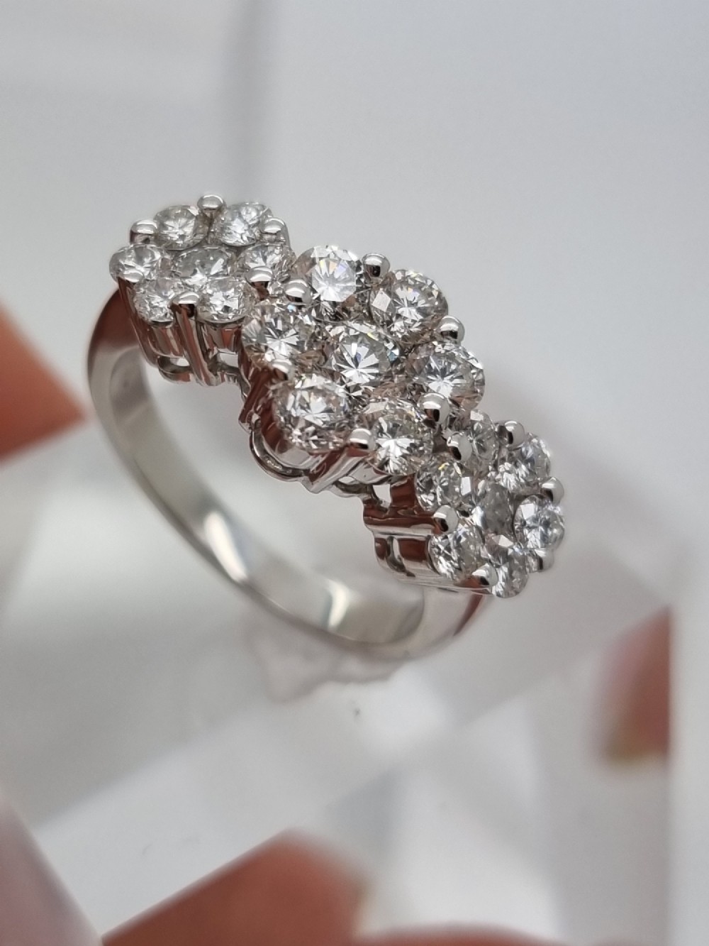 A platinum ring featuring three distinct floral cluster settings mounted with round brilliant diamonds on a smooth band.