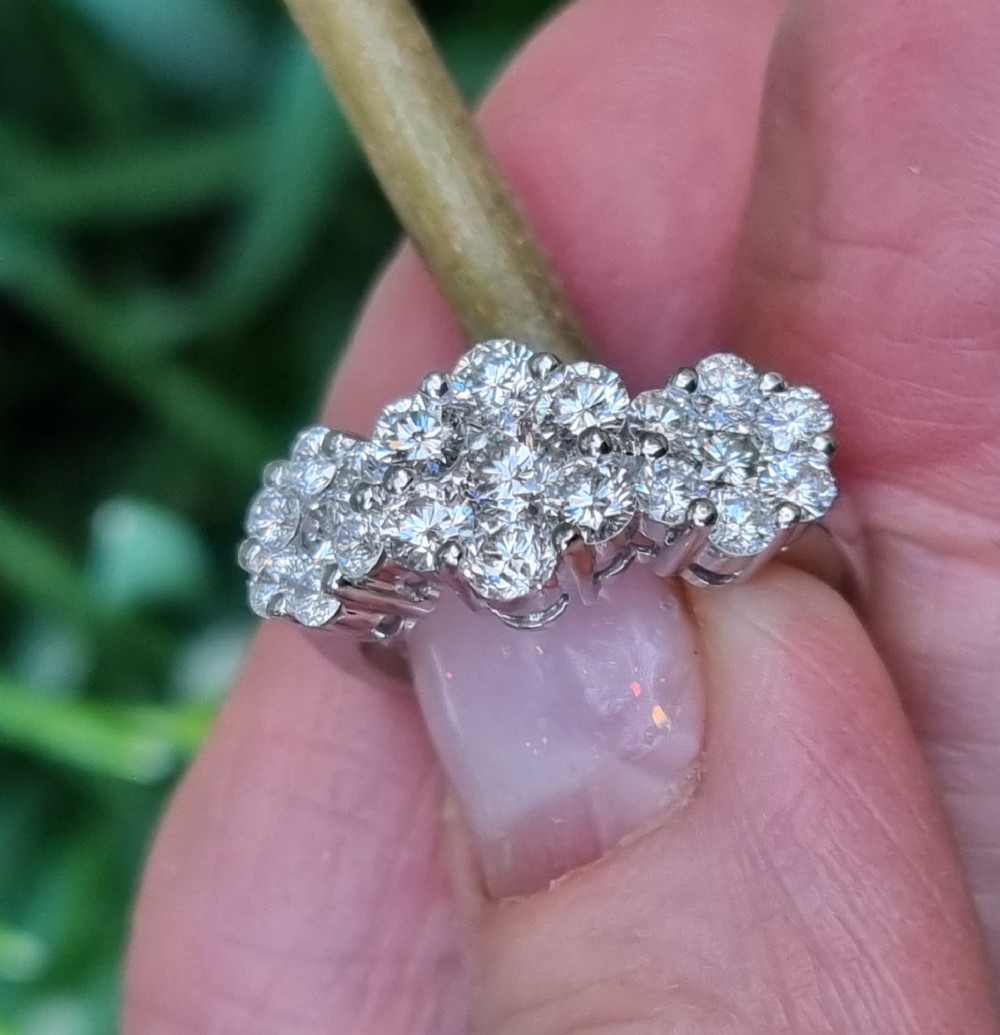 A platinum ring featuring three distinct floral cluster settings mounted with round brilliant diamonds on a smooth band. View V