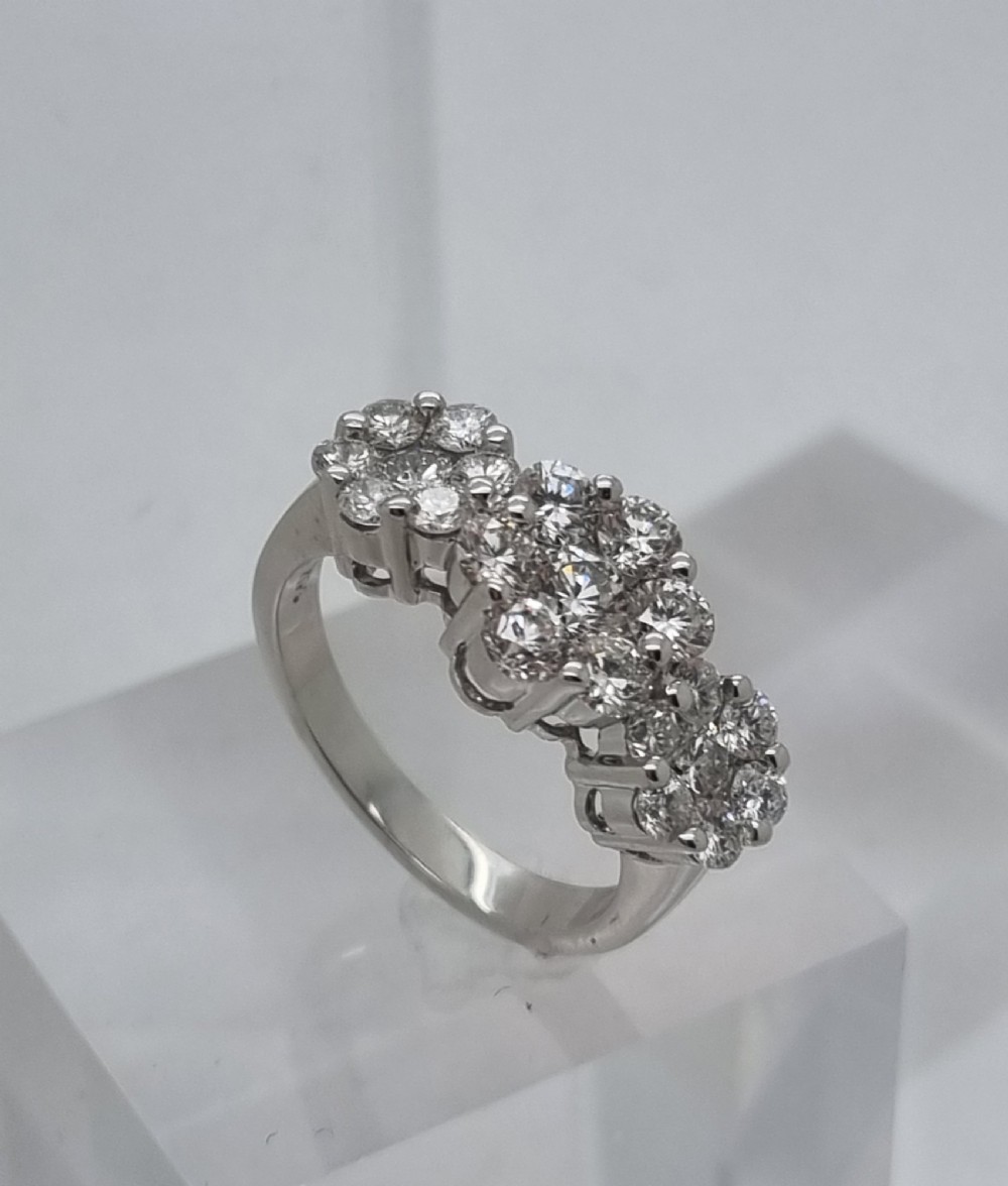 A platinum ring featuring three distinct floral cluster settings mounted with round brilliant diamonds on a smooth band. View VI