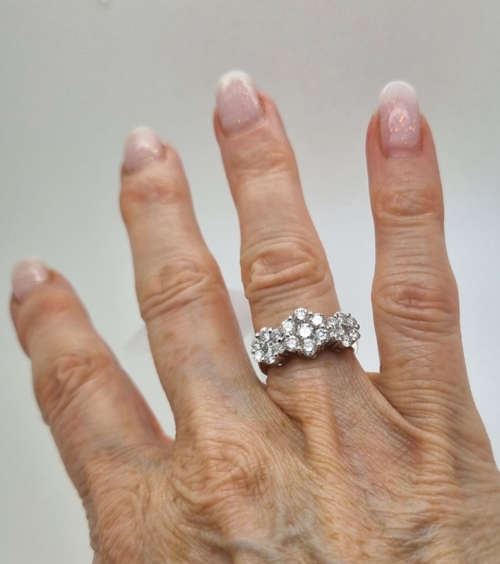 A platinum ring featuring three distinct floral cluster settings mounted with round brilliant diamonds on a smooth band. View VIII
