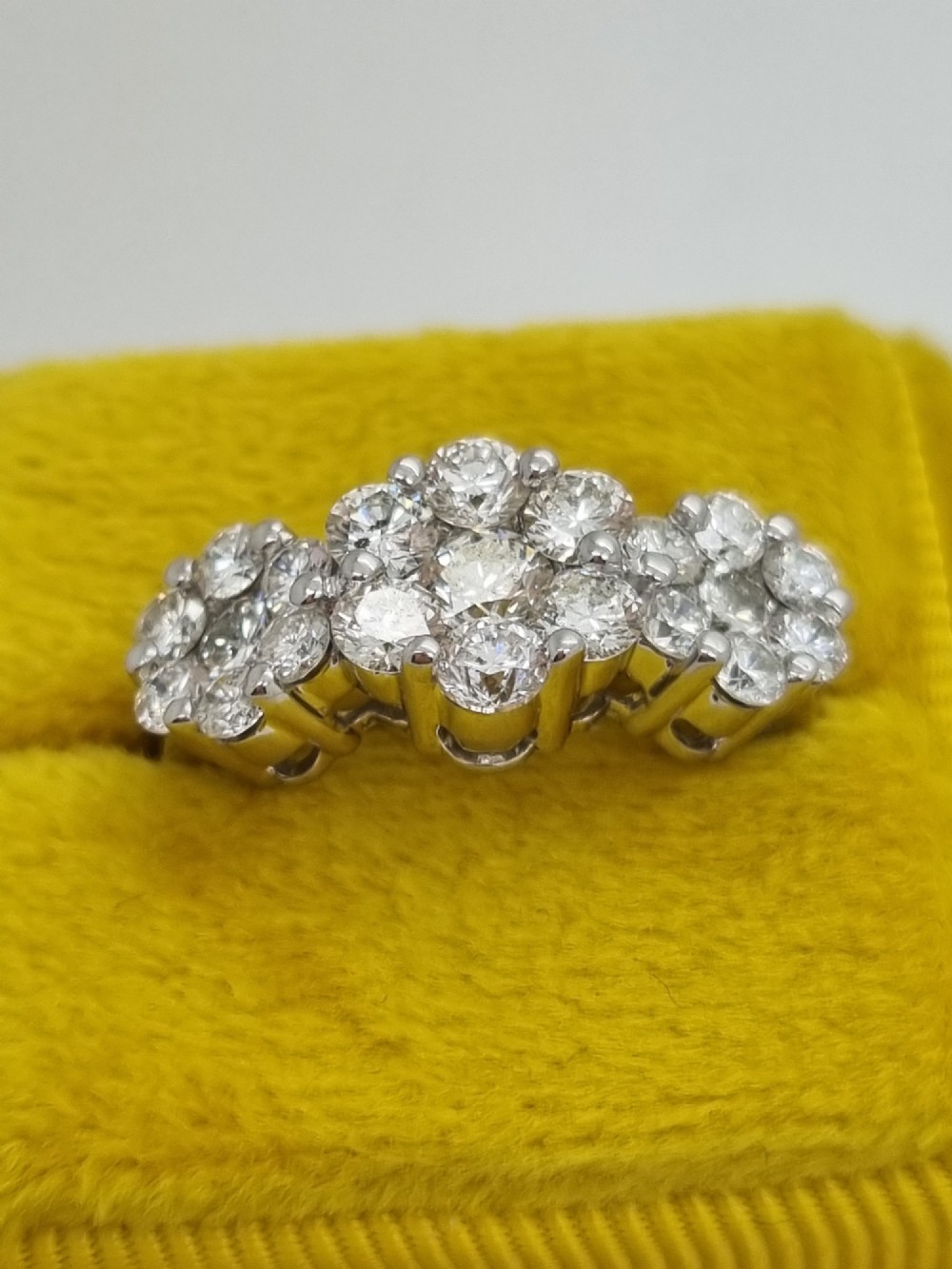 A platinum ring featuring three distinct floral cluster settings mounted with round brilliant diamonds on a smooth band. View IX