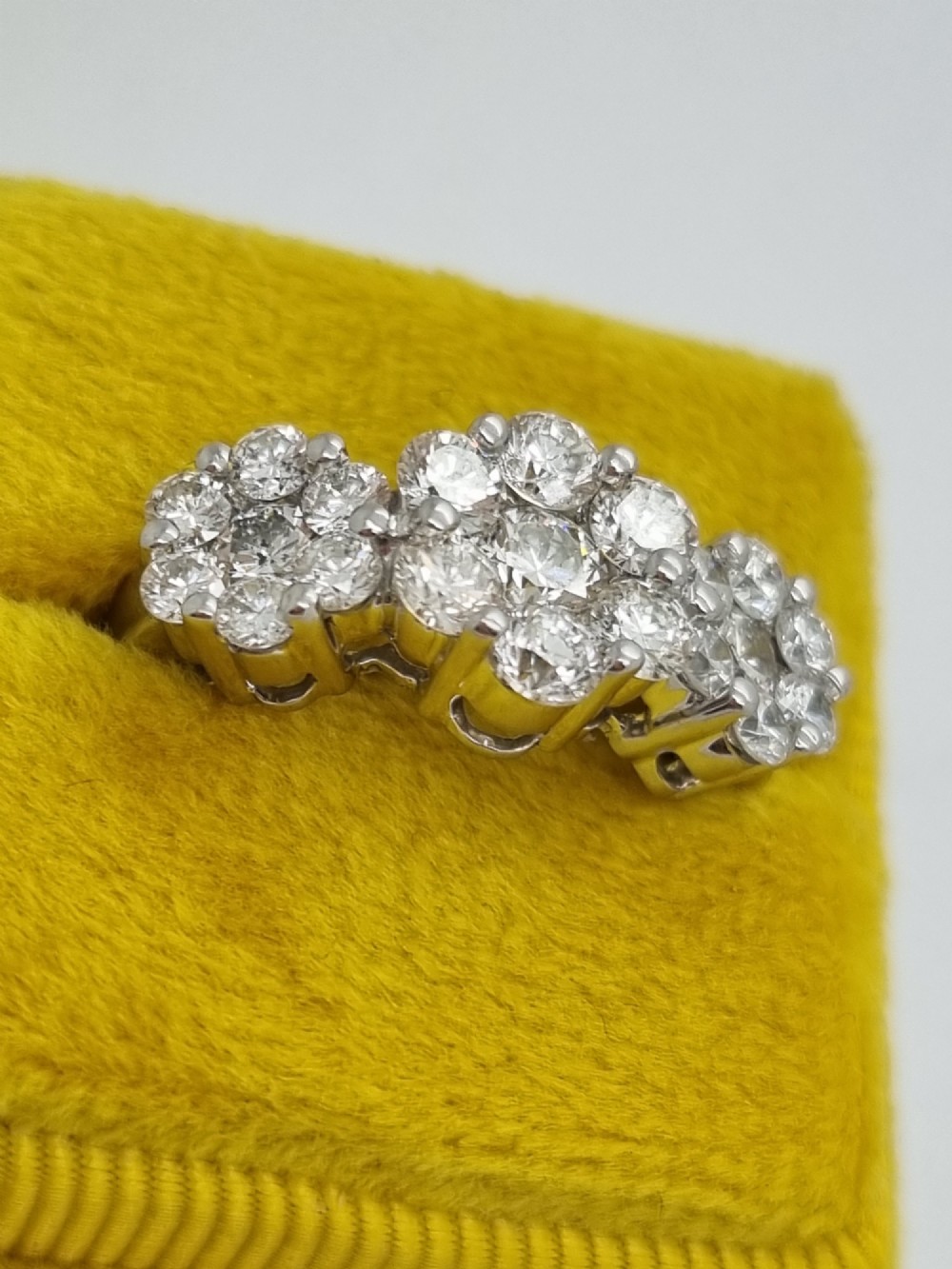 A platinum ring featuring three distinct floral cluster settings mounted with round brilliant diamonds on a smooth band. View X