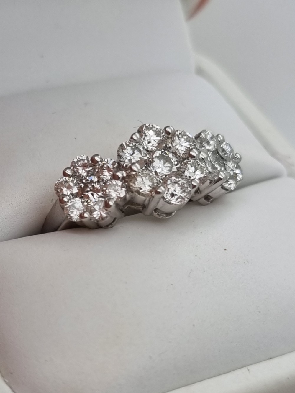 A platinum ring featuring three distinct floral cluster settings mounted with round brilliant diamonds on a smooth band. View XI