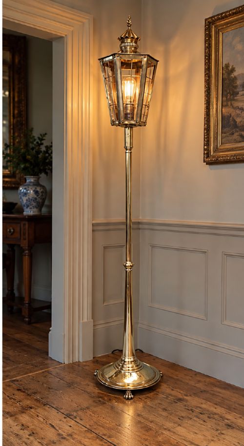 A tall, polished brass floor-standing lantern lamp featuring a hexagonal glass enclosure mounted on a slender turned stem and a circular stepped base with paw feet. View V
