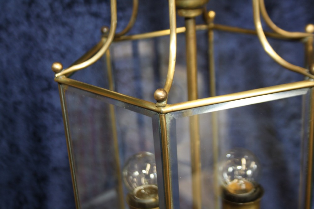 An early twentieth-century hexagonal brass hall lantern featuring six clear glass panels and a central light fixture suspended from a hooked top. View V