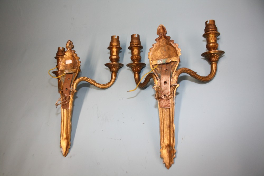 A pair of early 20th-century cast brass twin-arm wall lights featuring a cherub face motif and detailed foliate scrollwork. View II