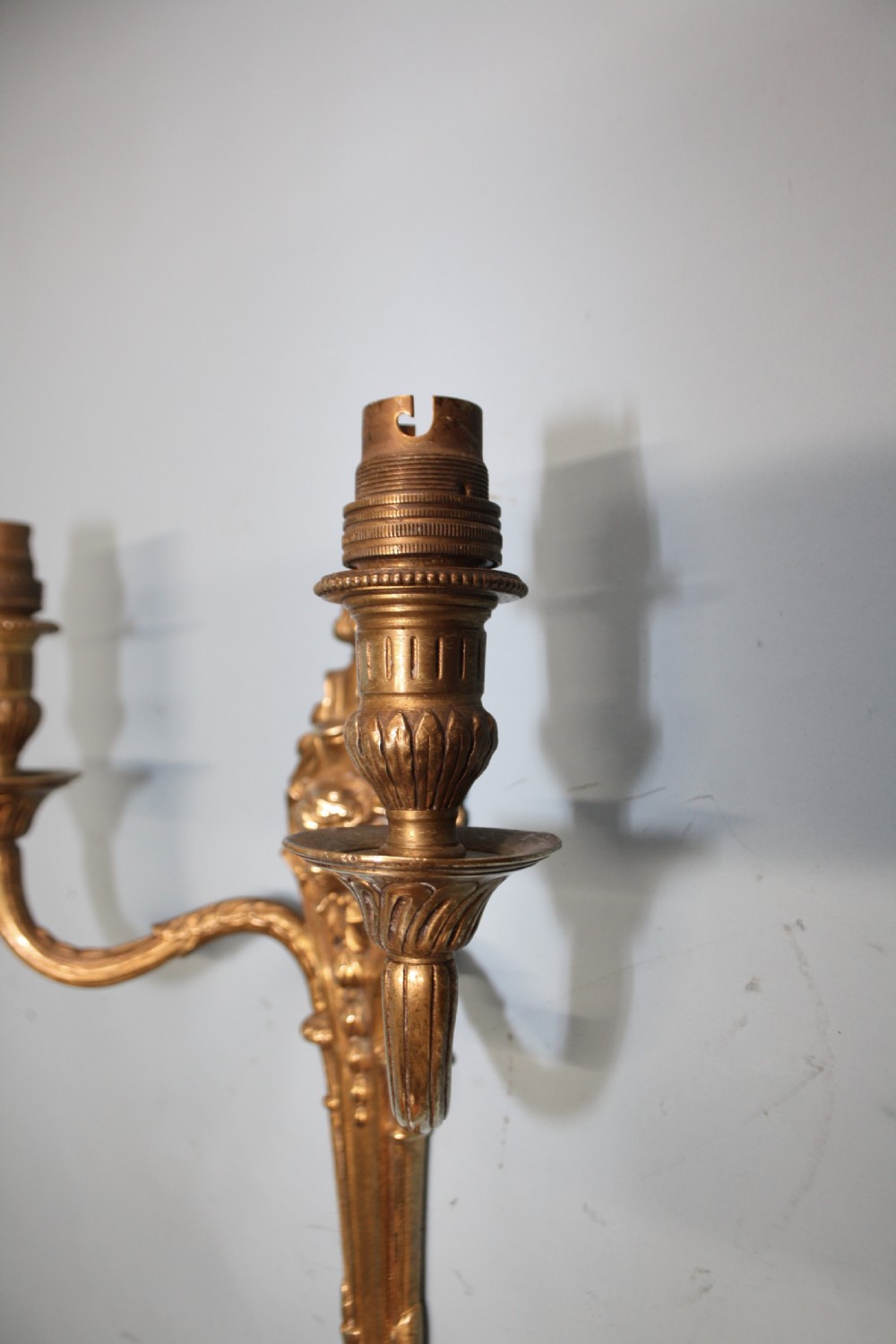 A pair of early 20th-century cast brass twin-arm wall lights featuring a cherub face motif and detailed foliate scrollwork. View III