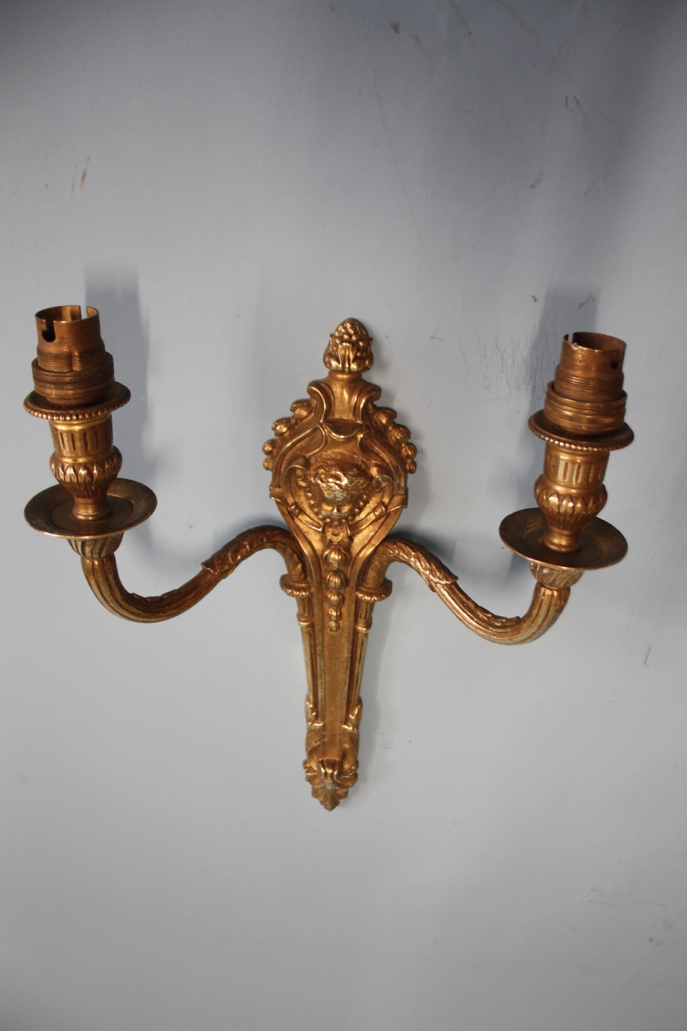 A pair of early 20th-century cast brass twin-arm wall lights featuring a cherub face motif and detailed foliate scrollwork. View V