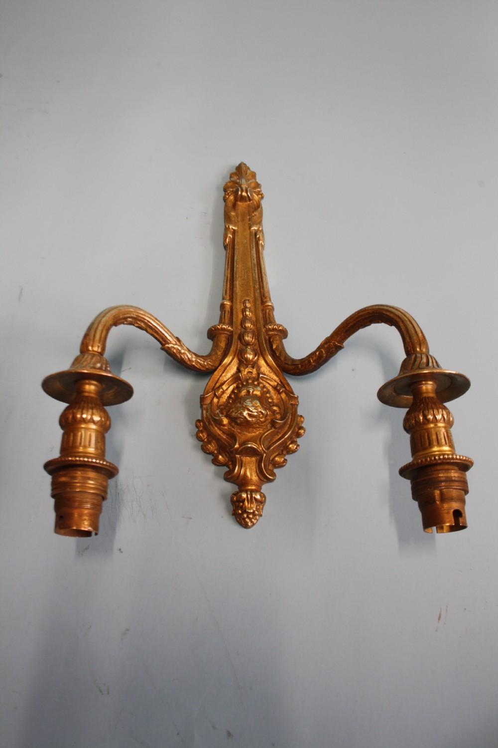 A pair of early 20th-century cast brass twin-arm wall lights featuring a cherub face motif and detailed foliate scrollwork. View VI