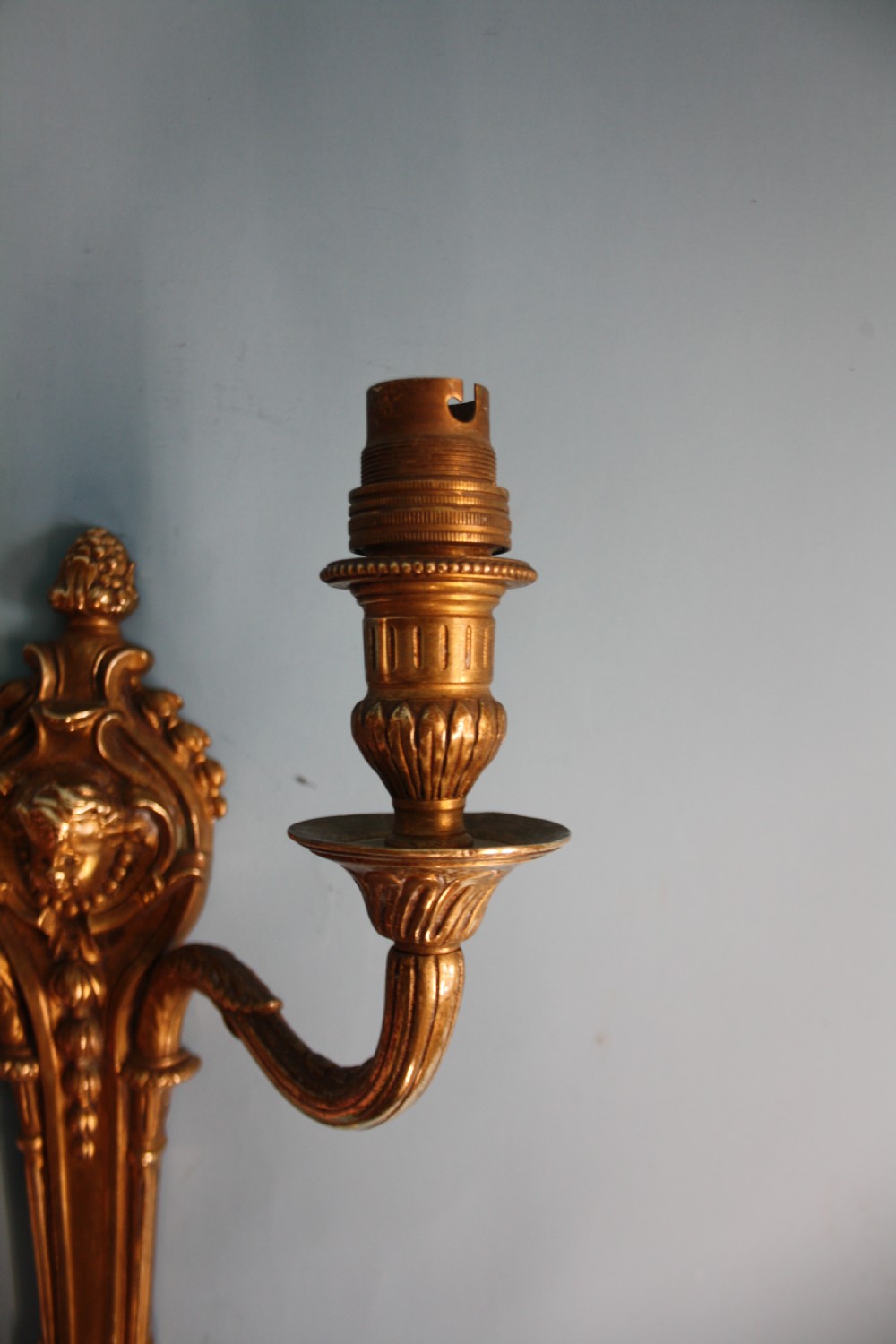 A pair of early 20th-century cast brass twin-arm wall lights featuring a cherub face motif and detailed foliate scrollwork. View VII