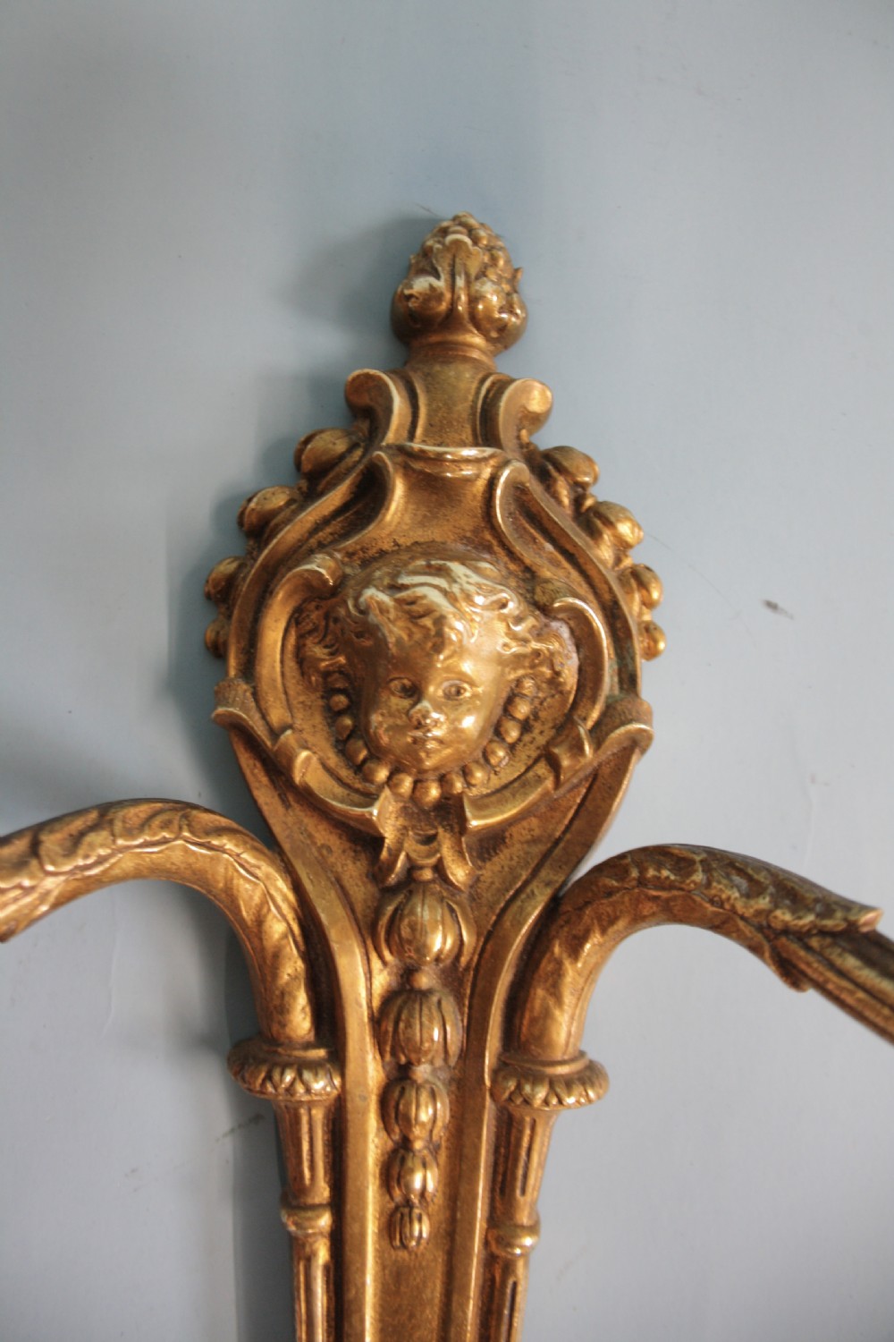 A pair of early 20th-century cast brass twin-arm wall lights featuring a cherub face motif and detailed foliate scrollwork. View VIII