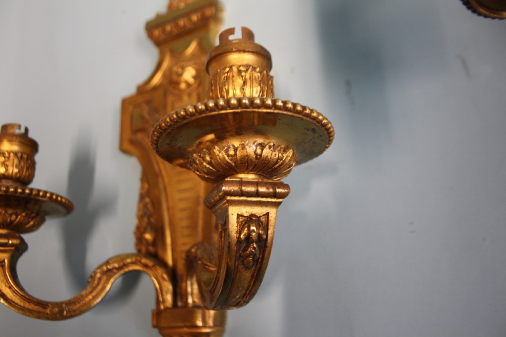 A pair of early 20th-century cast brass twin-arm wall sconces featuring Neoclassical garland and wreath embellishments. View III