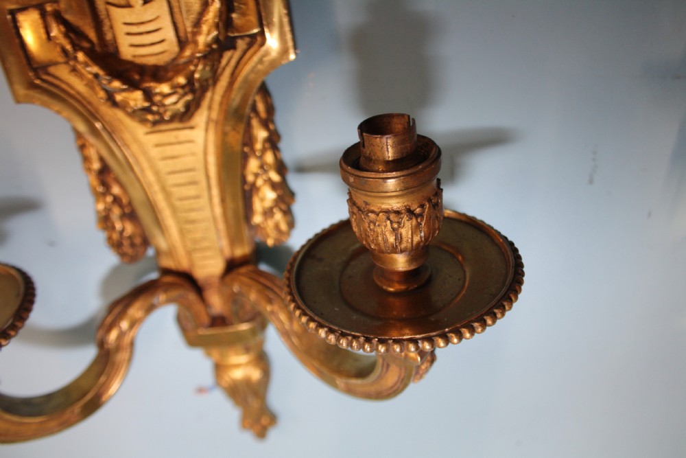 A pair of early 20th-century cast brass twin-arm wall sconces featuring Neoclassical garland and wreath embellishments. View IV