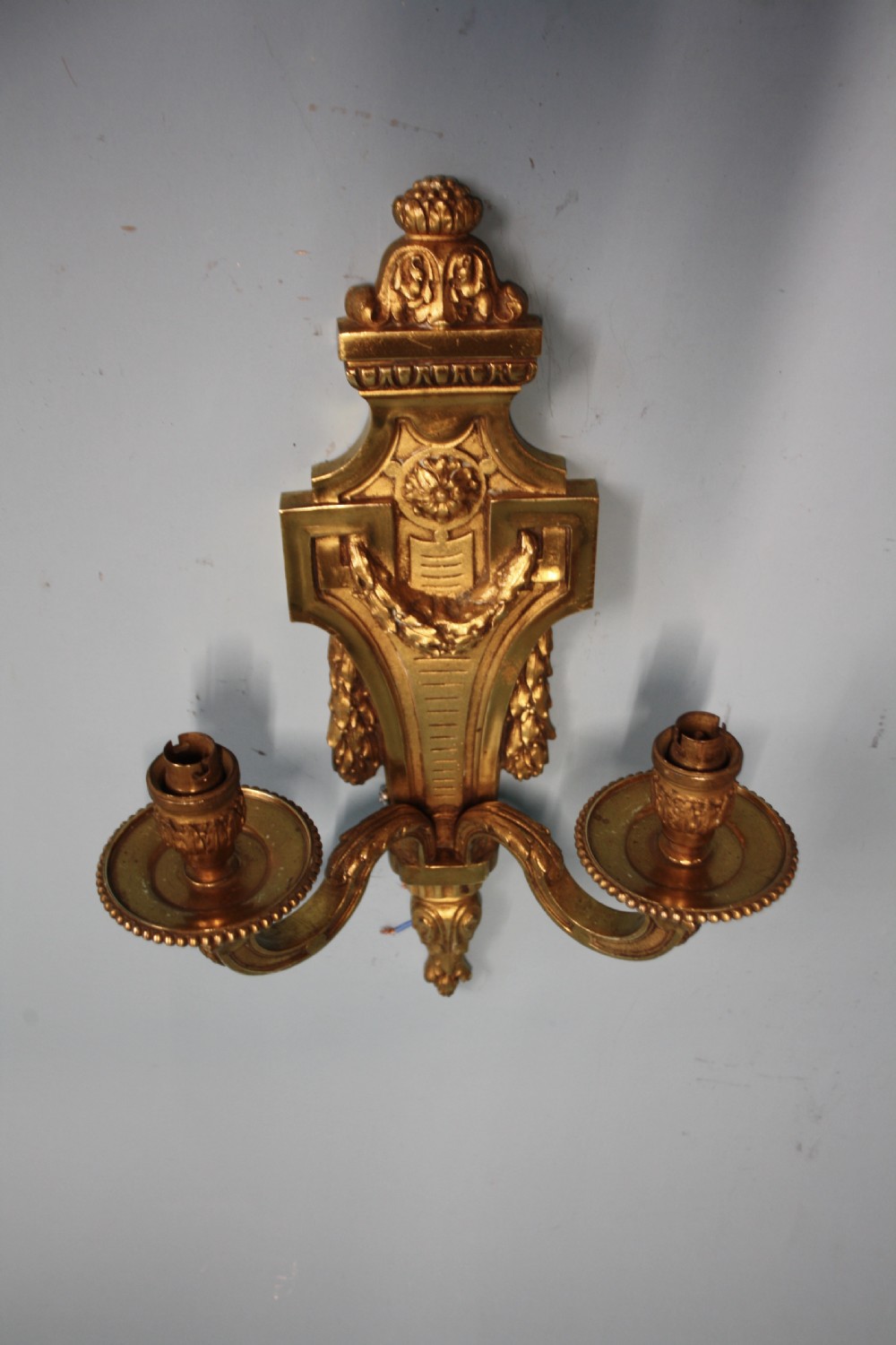 A pair of early 20th-century cast brass twin-arm wall sconces featuring Neoclassical garland and wreath embellishments. View V
