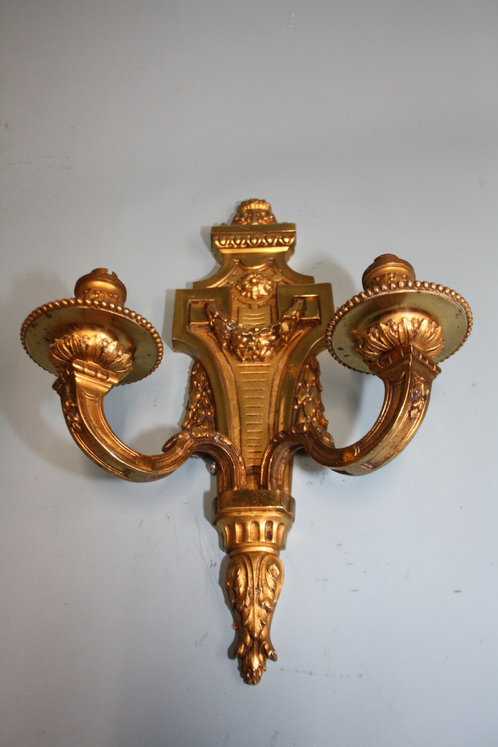 A pair of early 20th-century cast brass twin-arm wall sconces featuring Neoclassical garland and wreath embellishments. View VI